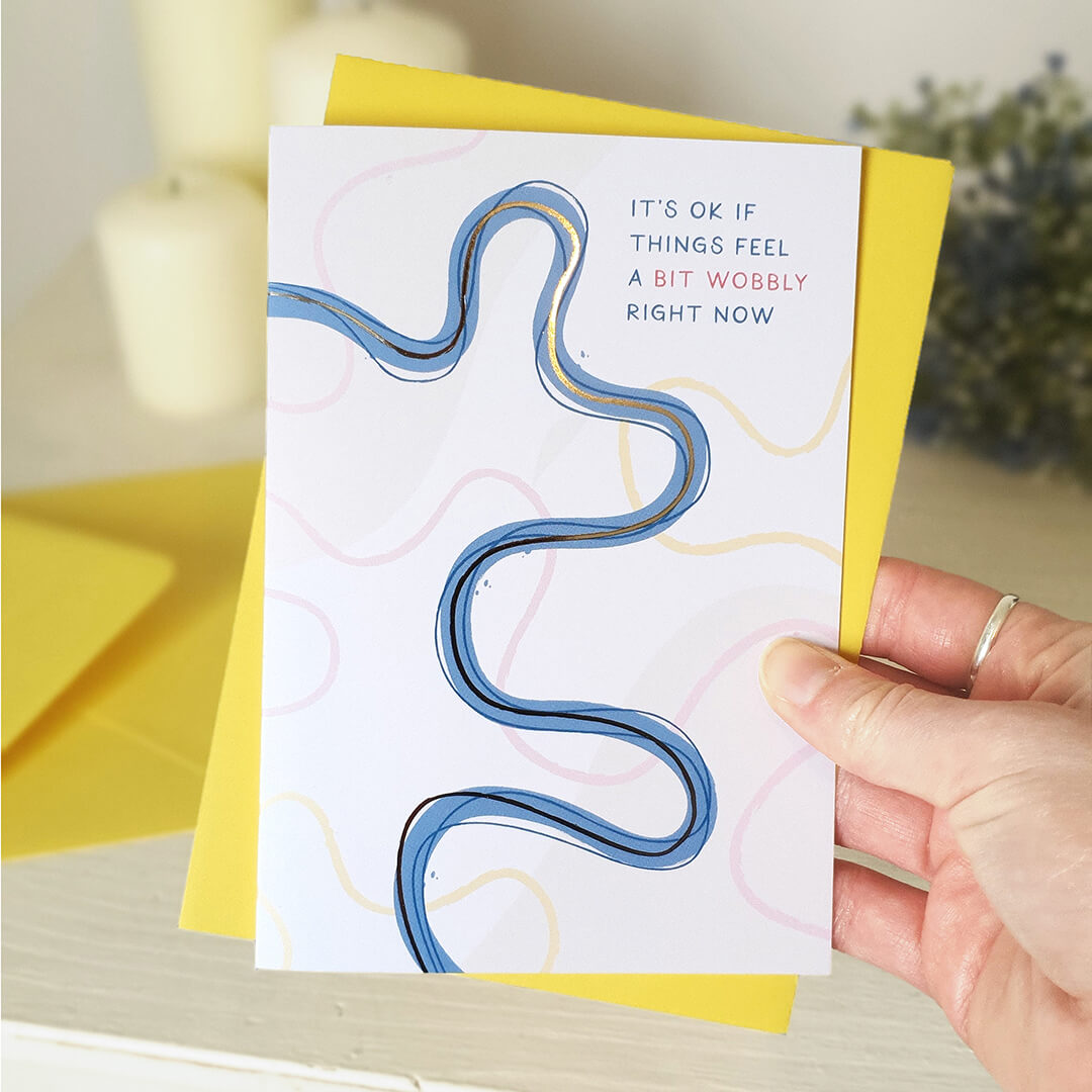 Hand holding a card with a blue wavy line design and text, set against a blurred indoor background.