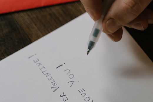 Hand holding writing pen, writing a Valentine's Day card, on a dark wooden table
