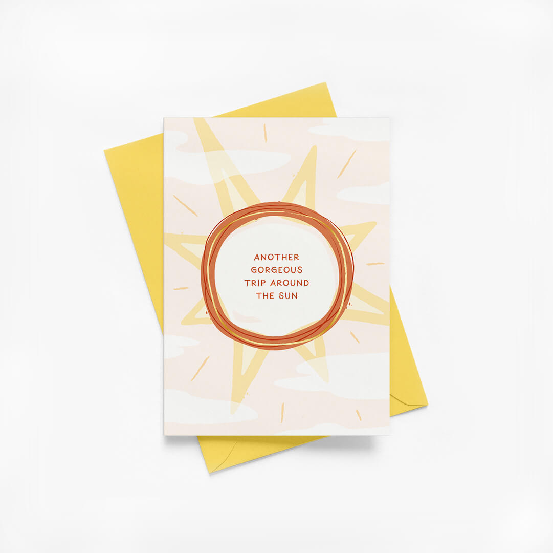 Birthday card with sun illustration, gold foil details and a yellow envelope on a white background