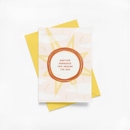 Birthday card with sun illustration, gold foil details and a yellow envelope on a white background