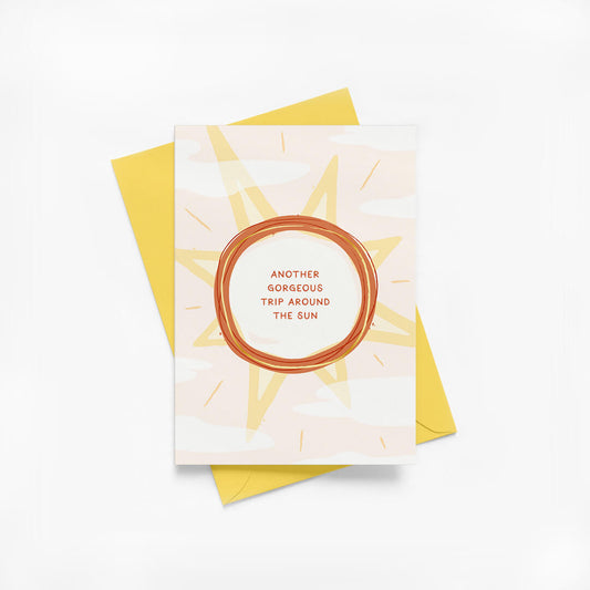 Birthday card with sun illustration, gold foil details and a yellow envelope on a white background