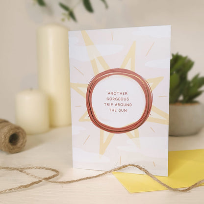 Birthday card with sun design and text 'Another gorgeous trip around the sun' sat on a light cream dresser.