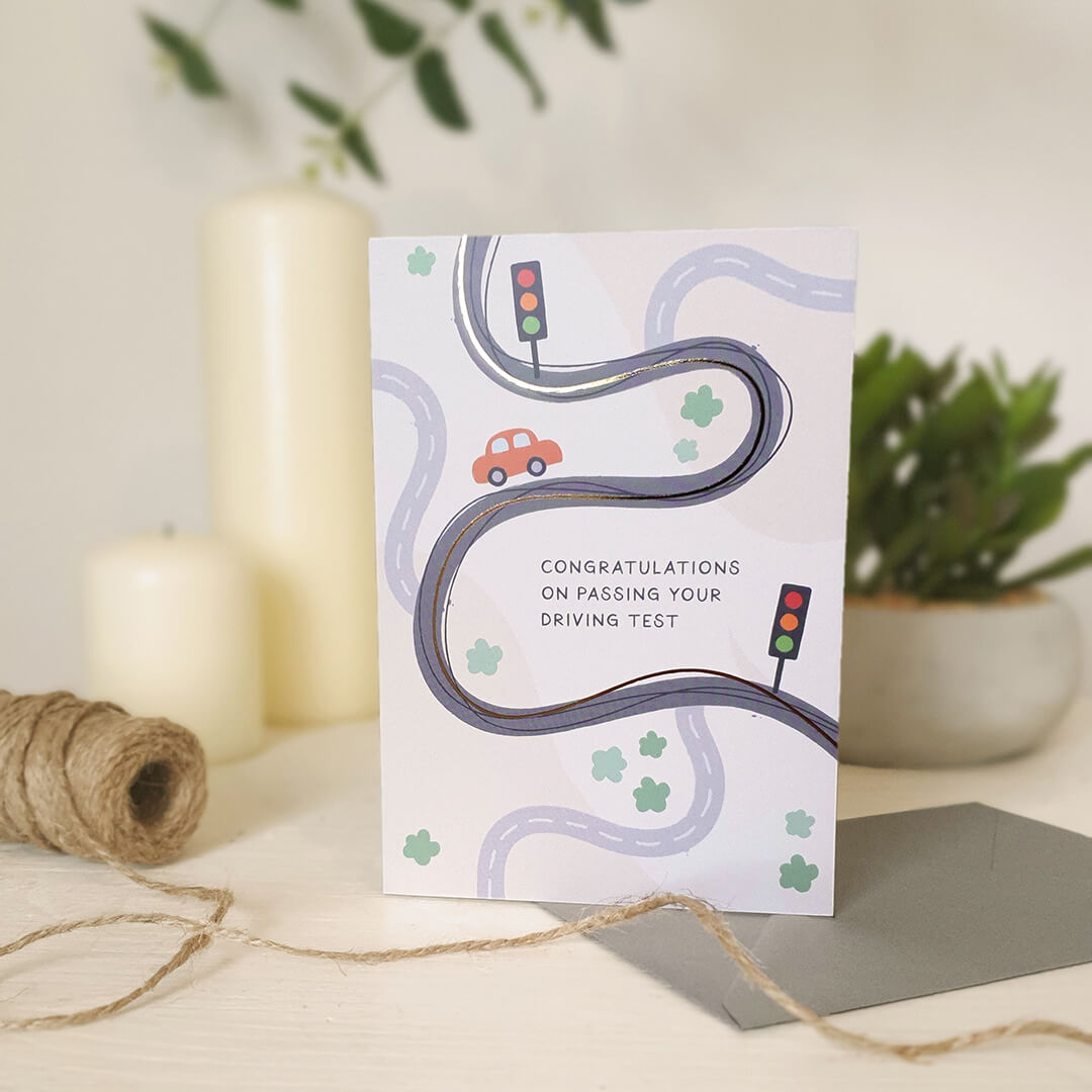Greeting card with road and traffic light illustrations on a light wooden dresser with candles and plants in the background