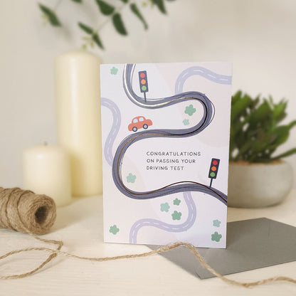 Greeting card with road and traffic light illustrations on a light wooden dresser with candles and plants in the background