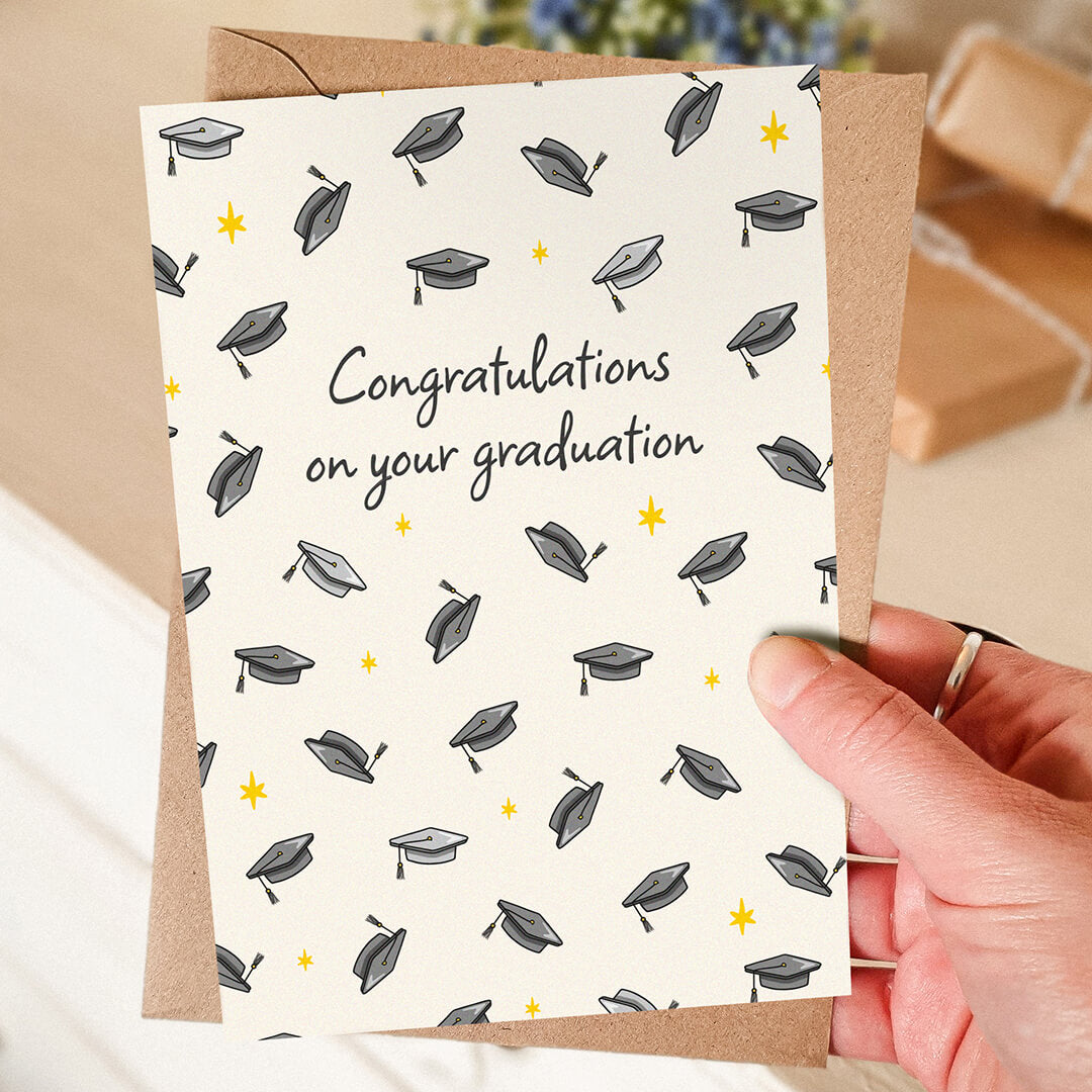 hand holding unique graduation card featuring illustrated mortarboards and a 'congratulations on your graduation' message with a blurred background
