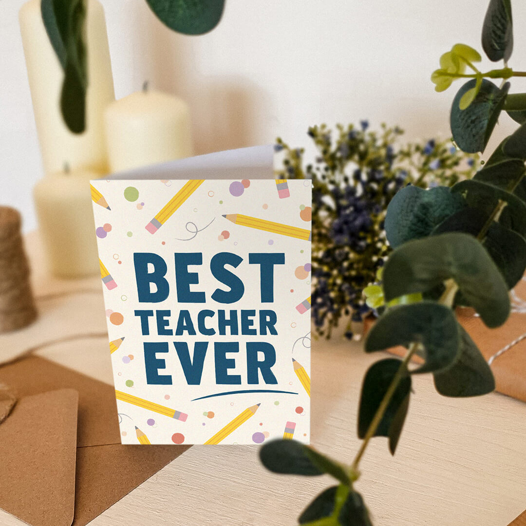 fun illustrated teacher card with best teacher ever message sat on a cream wooden dresser surrounded by candles and plants