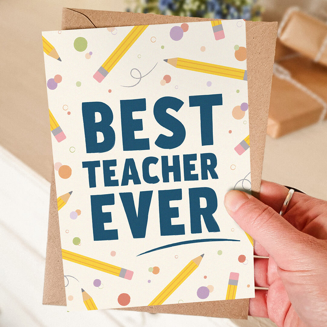 hand holding unique teacher card with best teacher ever message and pencil illustrations with a blurred background