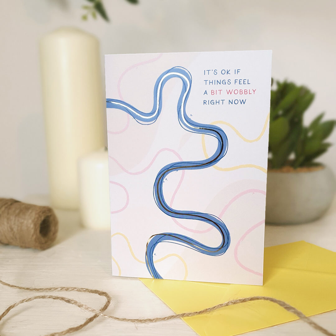 Mental health card with wavy line design and text on a light wooden dresser with a candle and plant in the background