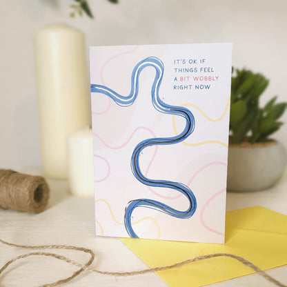 Mental health card with wavy line design and text on a light wooden dresser with a candle and plant in the background
