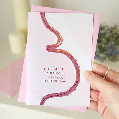 Hand holding a pregnancy card with a pink and white abstract illustration of a female body with a pink envelope.