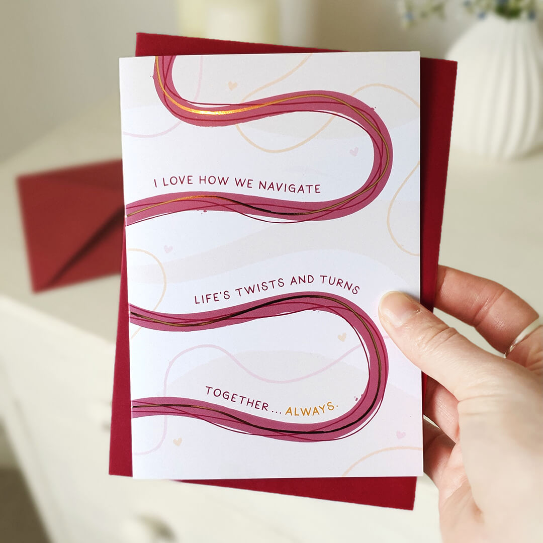Anniversary card with wavy lines and romantic text held by a hand, with a red envelope.
