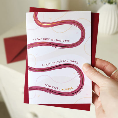 Anniversary card with wavy lines and romantic text held by a hand, with a red envelope.