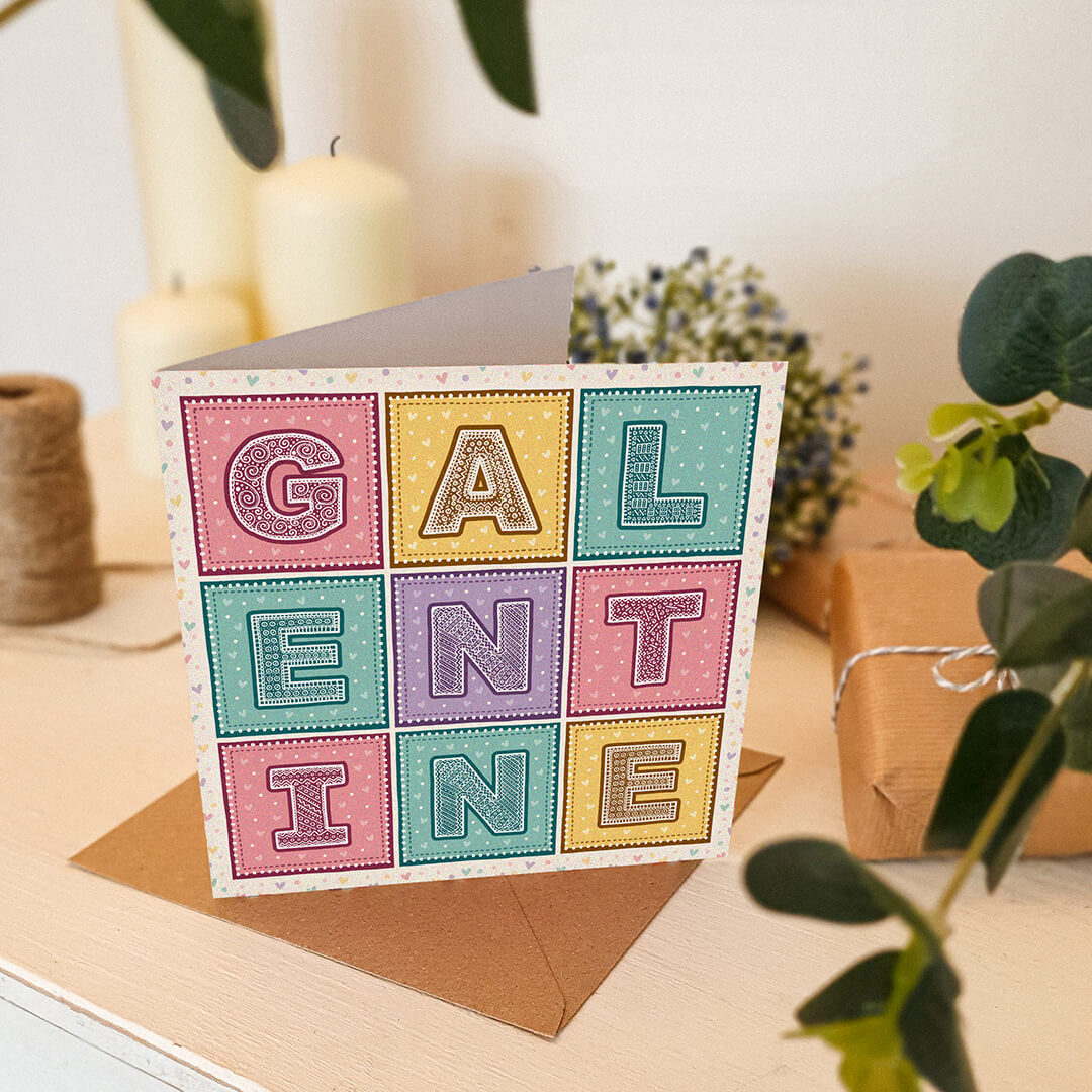 Cute pastel Galentine's Day card sat on white dresser surrounded by gifts, flowers and candles