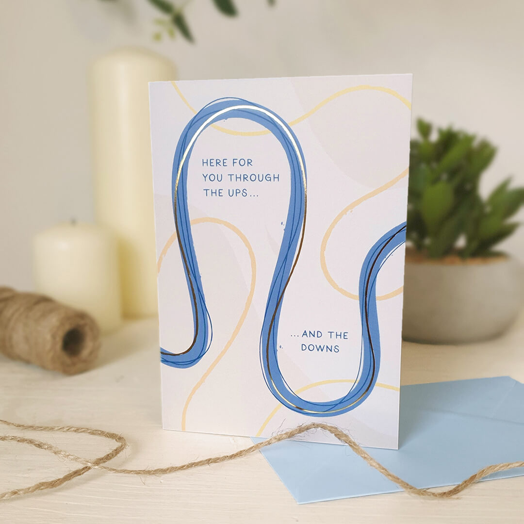 Friendship card with blue and yellow wavy line design on a light wooden dresser with plants and twine.