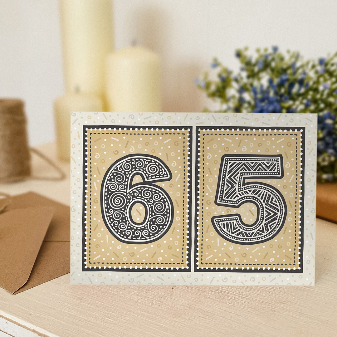 65th birthday card sat on a wooden shelf with candles and flowers in the background