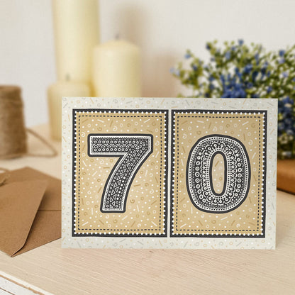 unique gold 70th birthday card with flowers and candles blurred in background