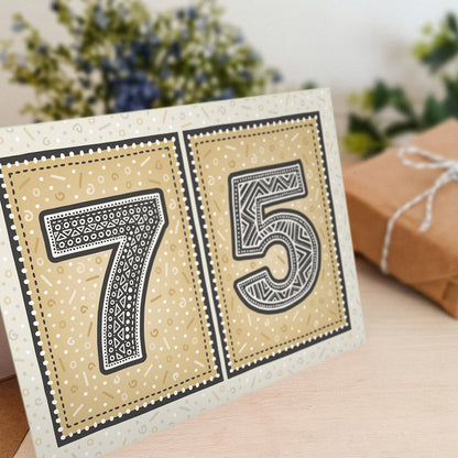 Special 75th birthday card sat on a wooden shelf with gifts and flowers in the background.