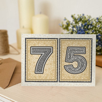 Gold 75th birthday card with a blurred background containing flowers and candles