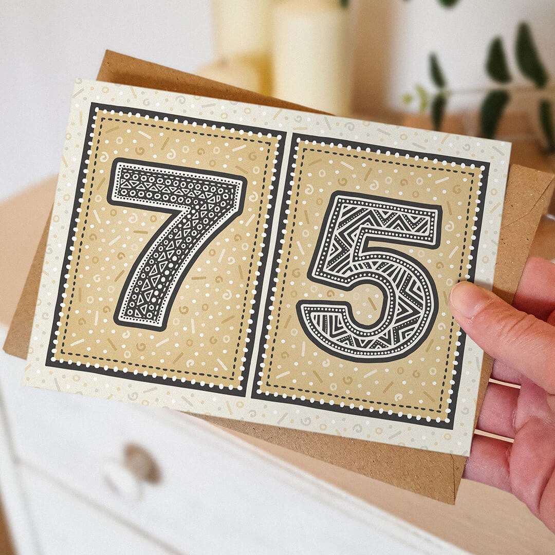 Hand holding a gold 75th birthday card, featuring decorative patterns.
