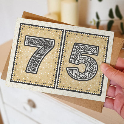 Hand holding a gold 75th birthday card, featuring decorative patterns.