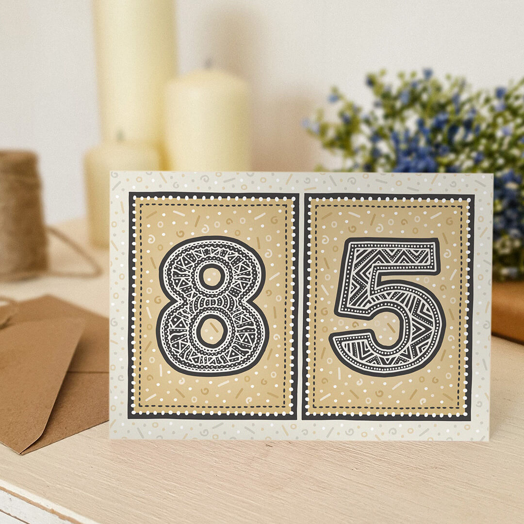 unique 85th birthday card sat on a wooden surface with candles and flowers in the background.