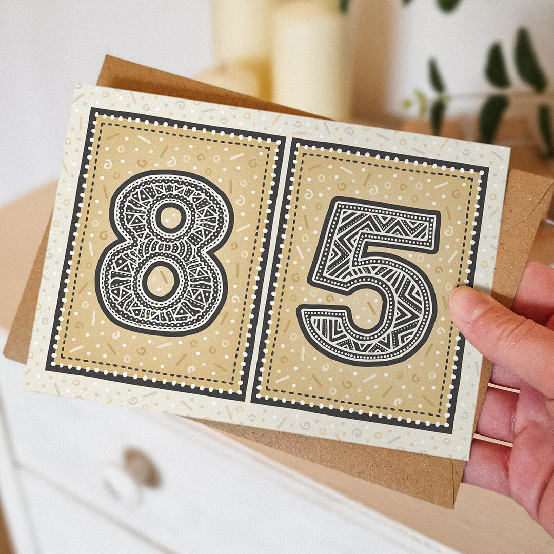 Gold 85th birthday card held by a hand against a blurred background