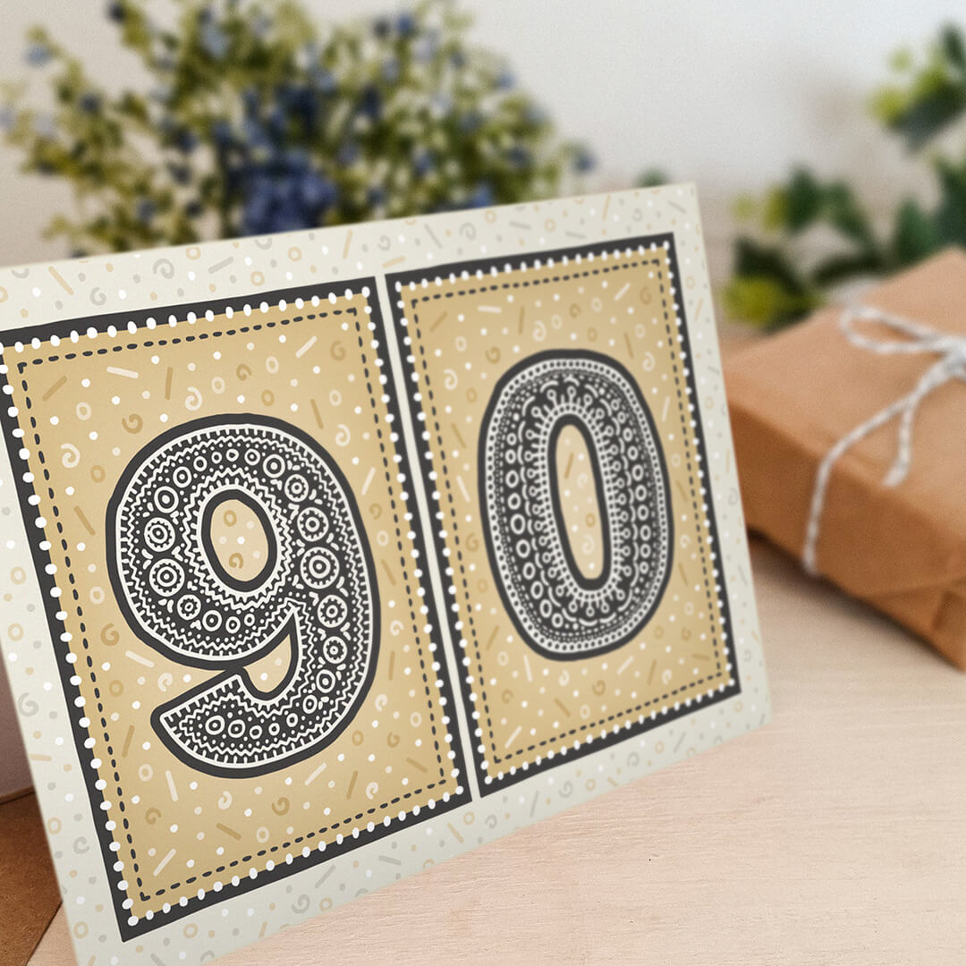 unique black and gold 90th birthday card with flowers and gifts in the background