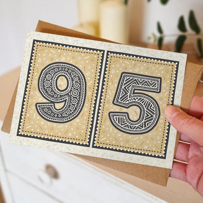 Hand holding a gold 95th birthday card against a blurred neutral background