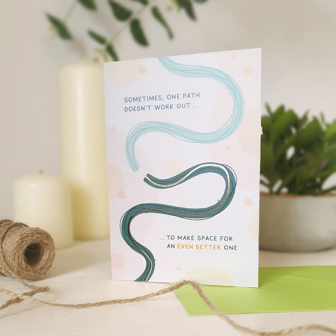 Motivational card with wavy lines and text on a light wooden dresser with plants and candles in the background