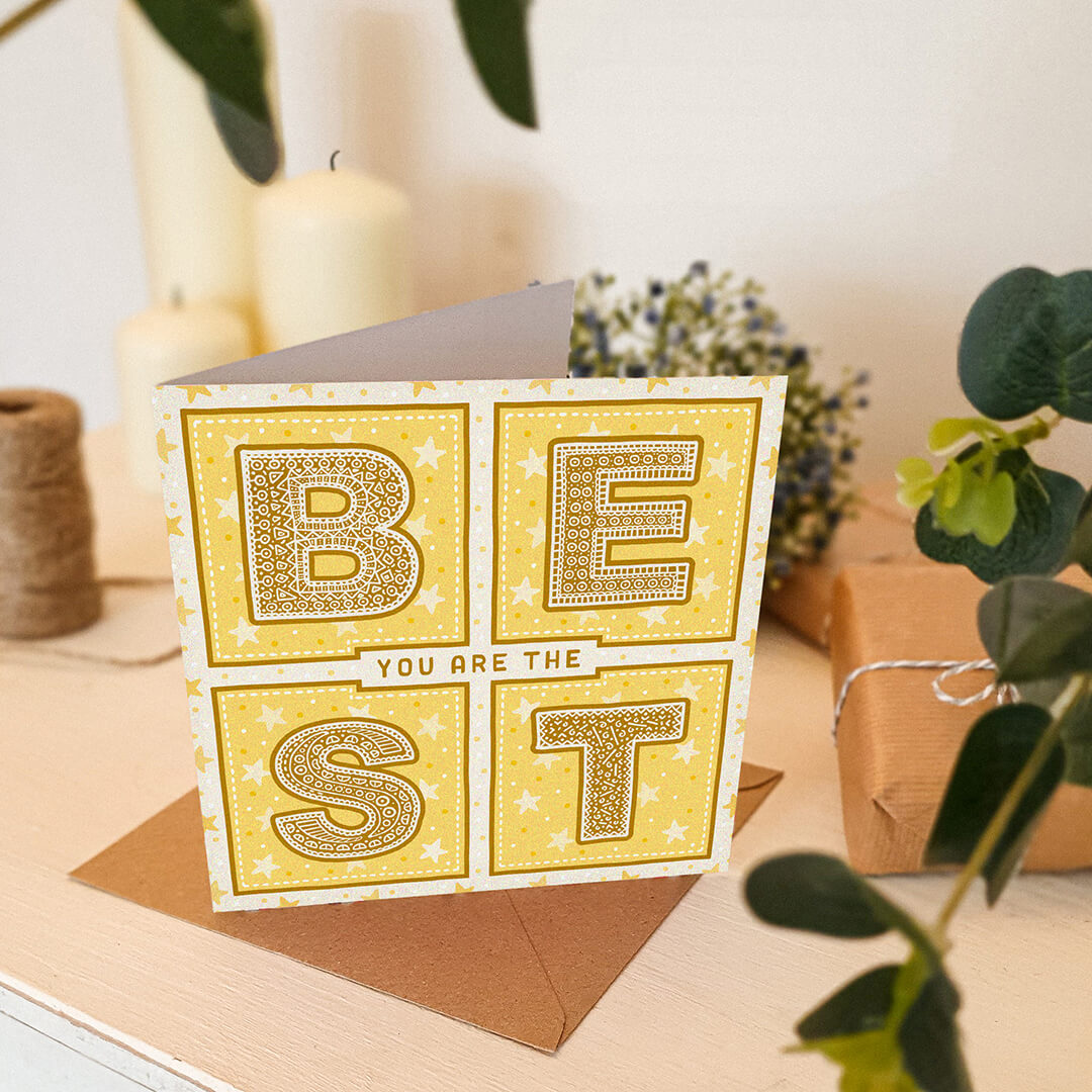 yellow thank you card with stars and you are the best message sat on a cream wooden dresser surrounded by plants and candles